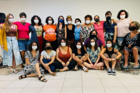 Foto com 19 integrantes da Rede de Colaboradoras, usando máscaras: 8 estão sentadas e 11 estão de pé e abraçadas umas às outras. Fim da descrição.