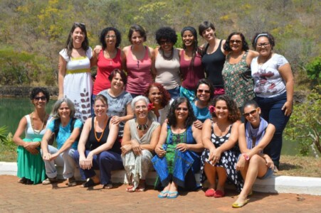 Fotografia de 18 mulheres com fundo com árvores.