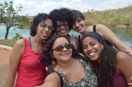 Fotografia de 5 mulheres abraçadas tirando foto em estilo selfie.