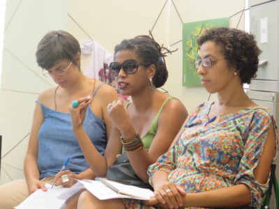 Foto de três mulheres. A do meio está gesticulando.